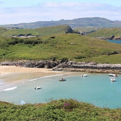 A sandy beach with mountains around it and boats in the cove