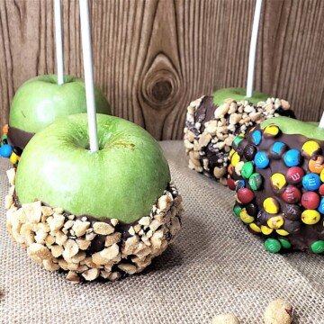 Four apples with lollipop sticks as holder and dipped in melted chocolate and decorate with crushed nuts or candies