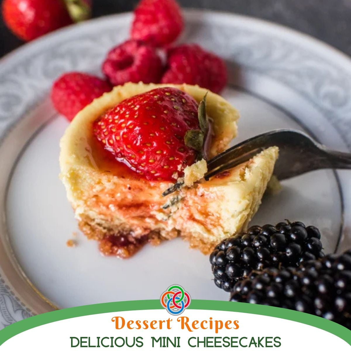 Close-up of a mini cheesecake topped with a fresh strawberry, served with raspberries and blackberries on a patterned plate with text banner.