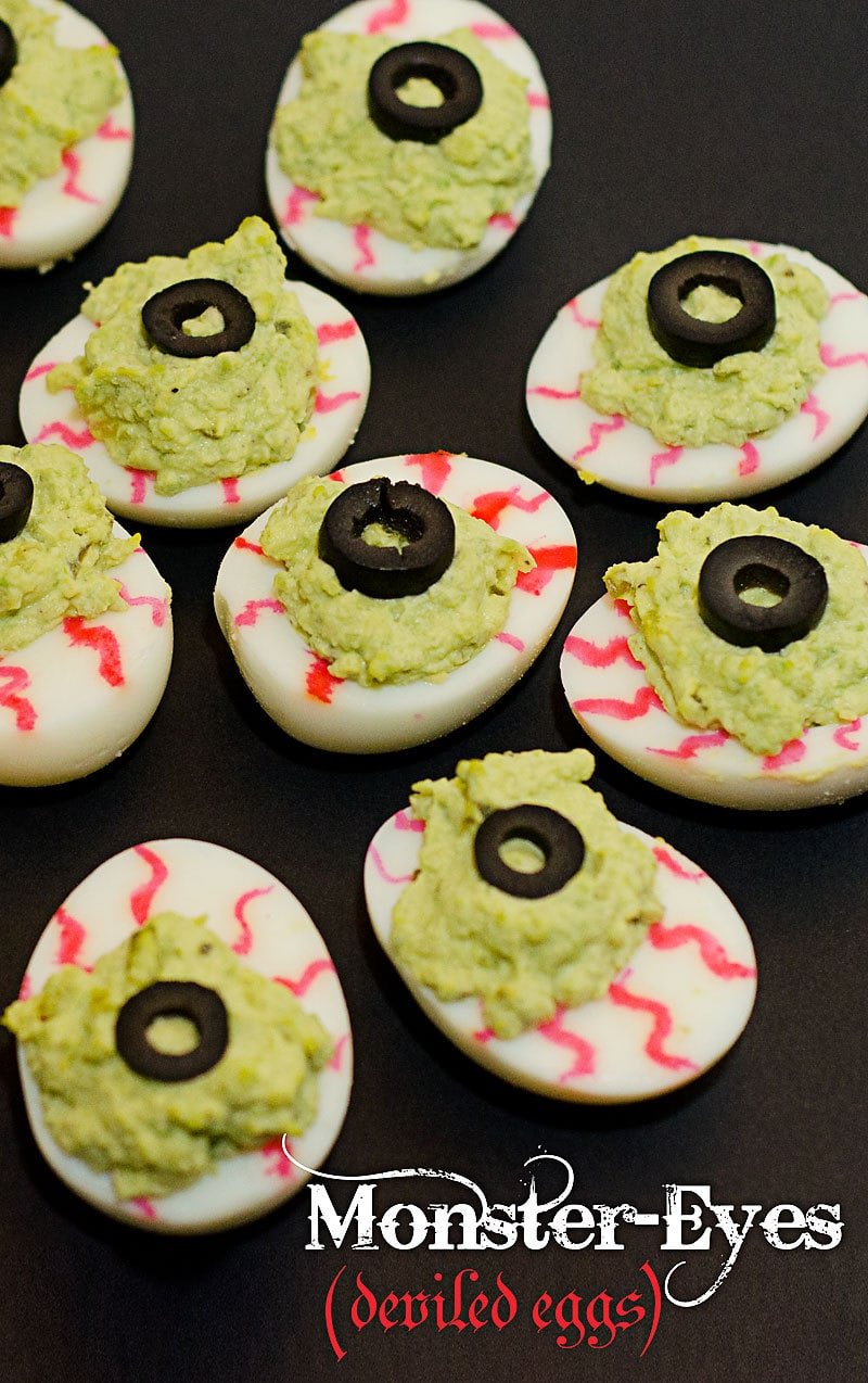 A plate of green devilled eggs with olives as monster eyes and red zig zags to look like bloodshot eyes