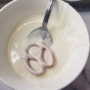 Using a spoon to dip a pretzel in a bowl of melted white chocolate