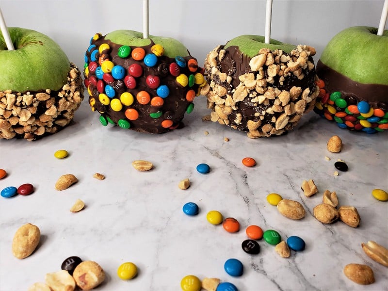 Four choclate dipped and decorated apples with lollipop sticks for holding them | Irish American Mom A row of chocolate dipped and decorated green apples with lollipop sticks inserted into them