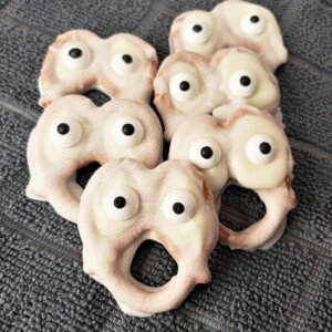White chocolate ghost pretzels with candy eyes displayed on a black dish cloth