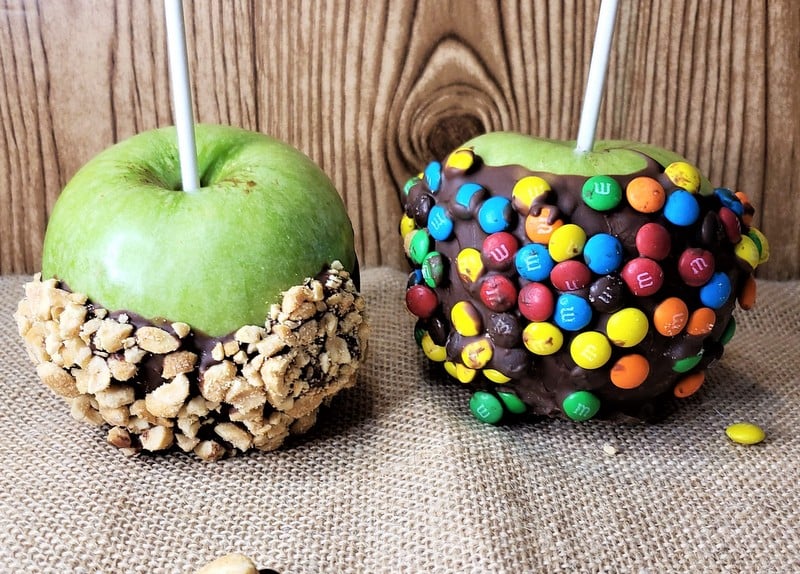 Two chocolate coated apples dipped in nuts and colorful candy | Irish American Mom Two chocolate dipped Halloween apples, one with crushed nuts and the other with colorful button candies as decoration