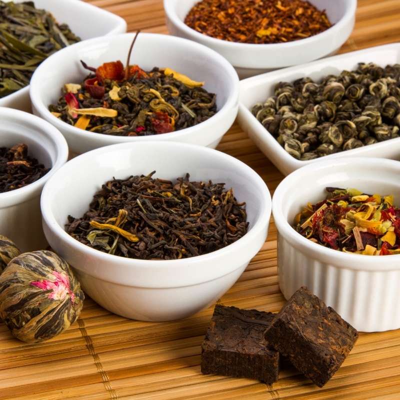 A selection of dried tea leaves | Irish American Mom White bowls of aromatic dried tea leaves displayed on a bamboo mat