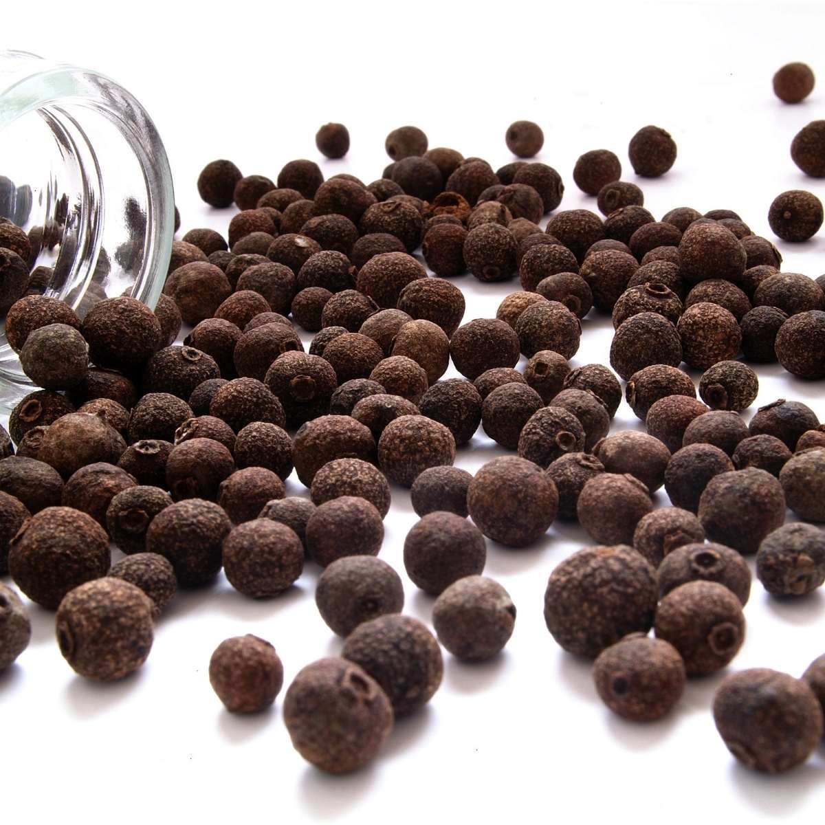 Allspice dried fruits spilled out of a glass mason gar on a white surface
