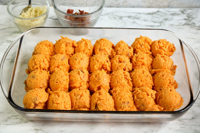 Even scoops of sweet potato in a dish for Twice Baked Sweet Potato Casserole with Bacon | Irish American Mom Scoops of sweet potato mixture in a glass casserole on a marble counter