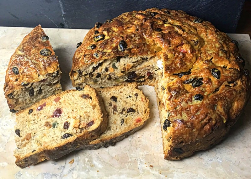 A loaf of Irish barmbrack fruited bread on a chopping board with two slices and the interior on display