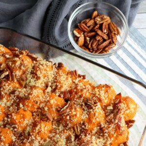Pecan topped sweet potato casserole in a glass dish beside a small bowl of pecans
