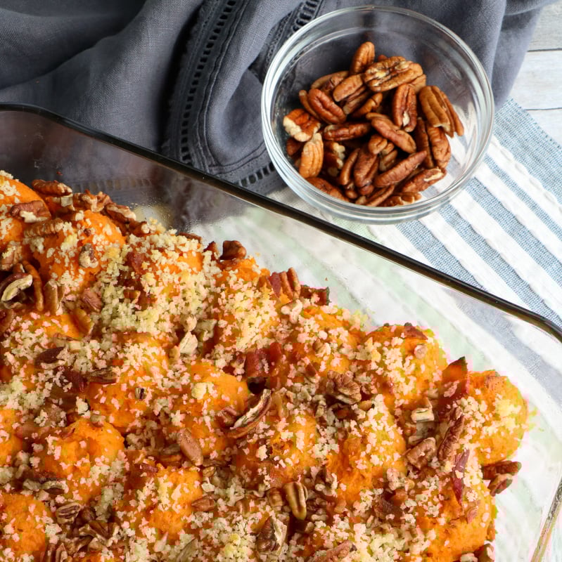 Twice Baked Sweet Potato Casserole with Bacon and pecan topping | Irish American Mom Pecan topped sweet potato casserole in a glass dish beside a small bowl of pecans