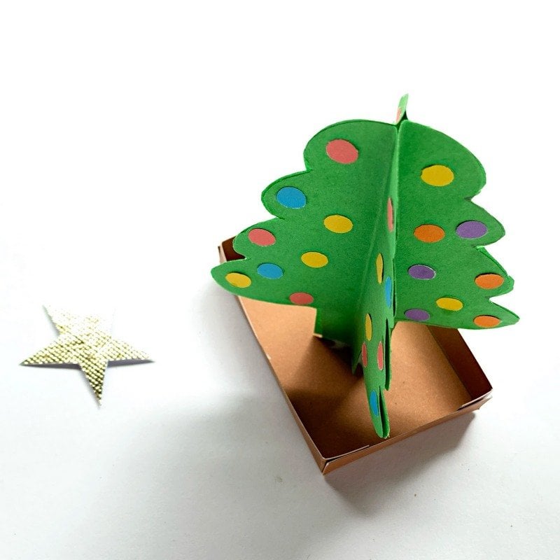 A star for a paper Christmas tree | Irish American Mom A green 3D paper Christmas tree on a brown box stand with a golden star lying beside it