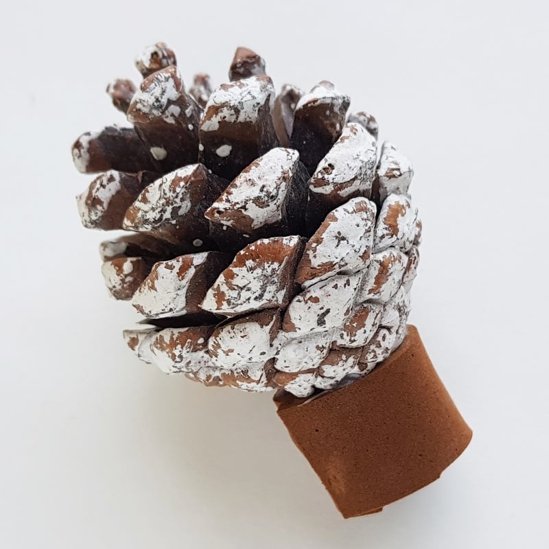 A pine cone sprayed with white craft snow on a foam tree trunk | Irish American Mom A pine cone with craft snow sprayed on it on top of a brown foam tree trunk