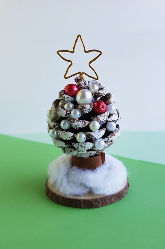 A single pine cone on a wooden disc decorated as a Christmas tree | Irish American Mom A pine cone with red and white beads and white paint to look like a Christmas tree displayed on a wooden disc