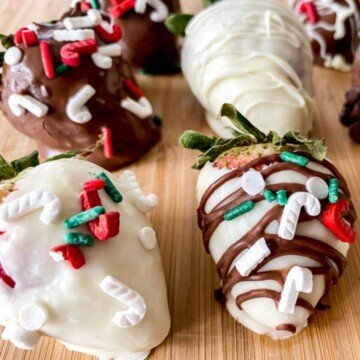 Four strawberries covered in melted chocolate with Christmas sprinkles