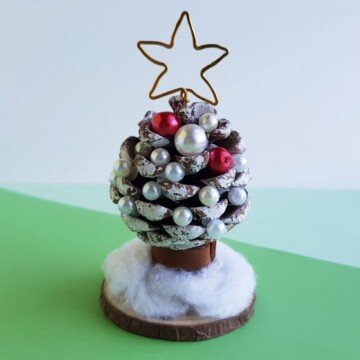 A pine cone Christmas tree on a small wooden circle on a green surface