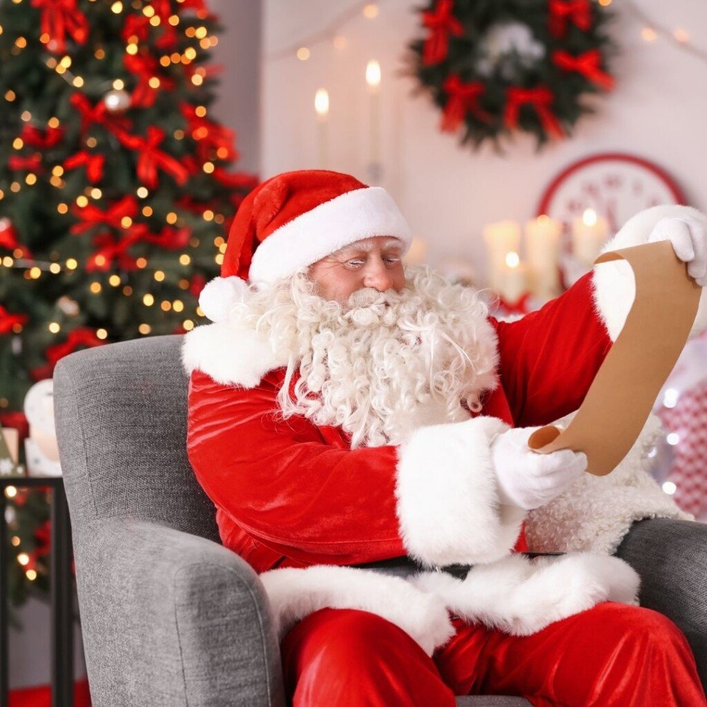 Santa Claus checking his list sitting in a chair beside a Christmas tree
