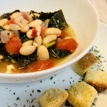 Diced tomato, white beans, kale and onions in broth in a white bowl