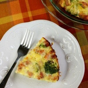 Slice of quiche with ham and broccoli on a white plate with a fork