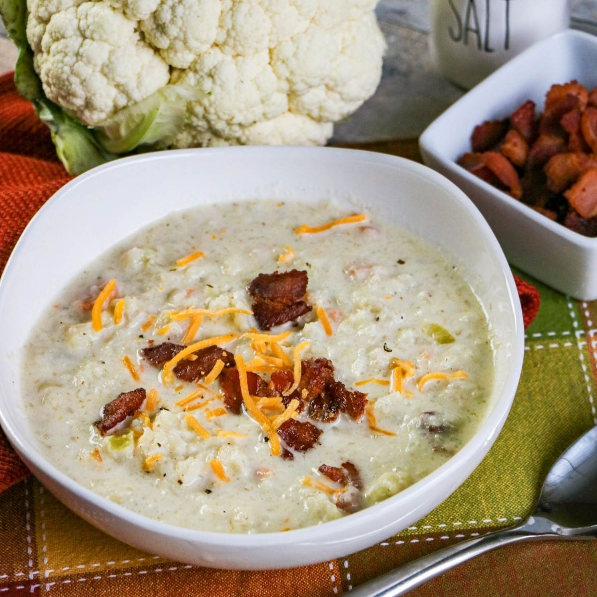 Cauliflower and bacon soup beside a cauliflower and bacon bits featured image | Irish American Mom Bacon bits on a bowl of cauliflower soup beside a bowl of bacon bits and a head of cauliflower