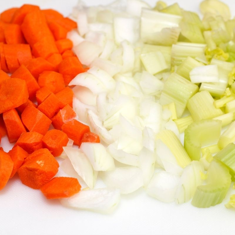 Sliced carrots, diced onion and chopped celery on a white surface