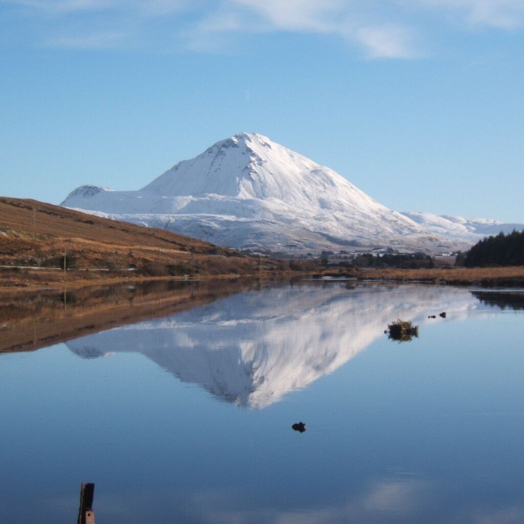A snowy mountain reflecting in a lake under a blue sky