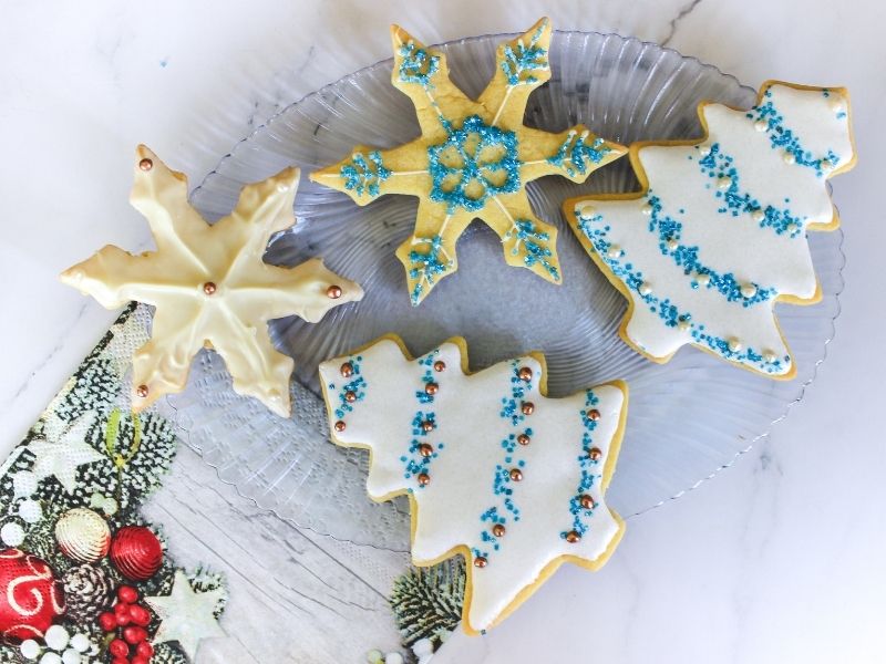 Christmas tree cookies and star cookies on a glass plate beside Christmas decorative foliage