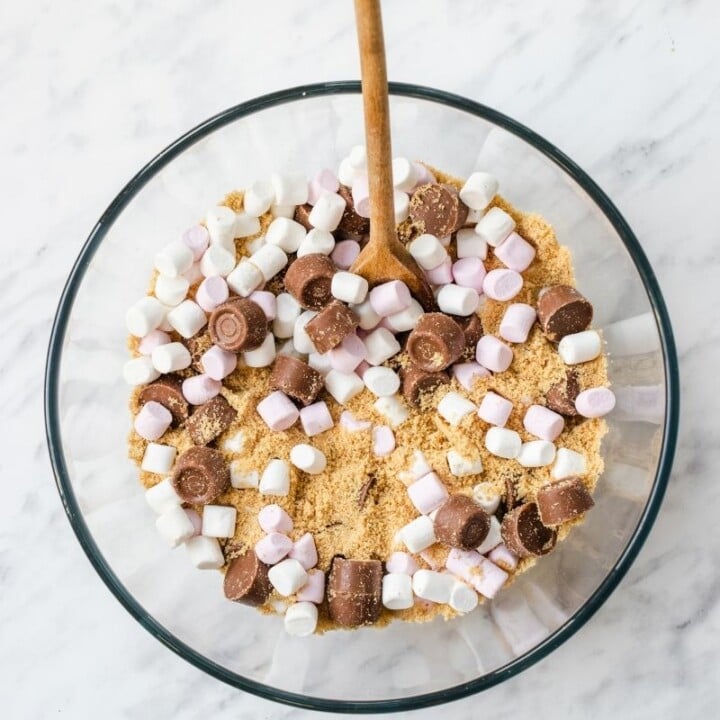 Combining biscuit crumbs, marshmallows and chocolate caramels for Rolo Rocky Roads | Irish American Mom Cookie crumbs, marshmallows and chocolate candy in a bowl with a spoon