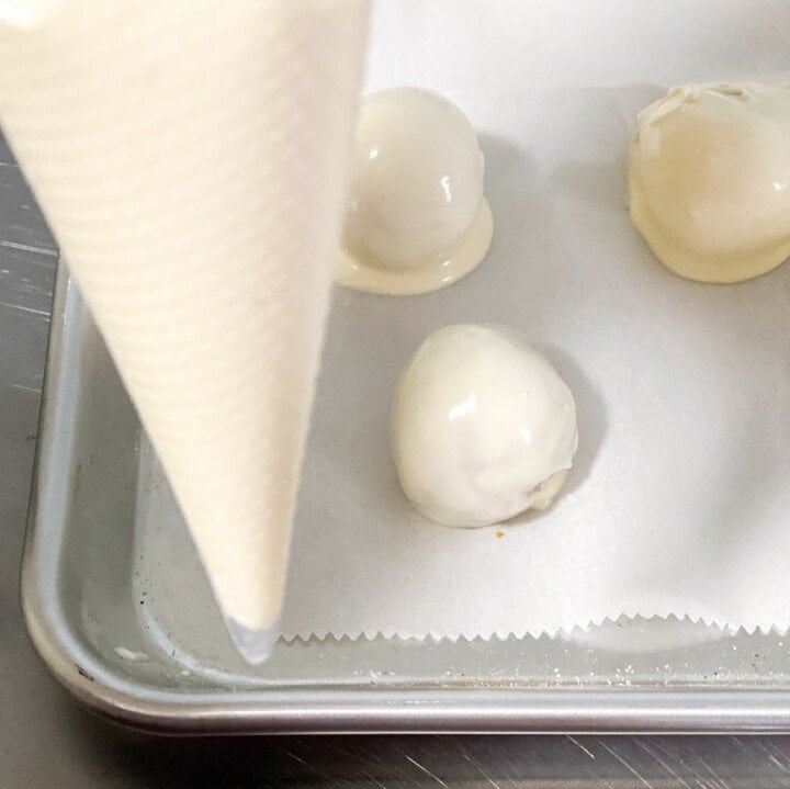 Covering cake truffles with white chocolate | Irish American Mom Using a piping bag of white chocolate to decorate truffles on a baking sheet