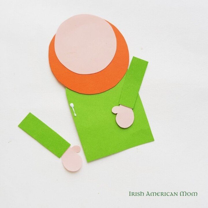 Gluing the leprechaun arms to the body for a bookmark | Irish American Mom Positioning paper arms on a paper cut out leprechaun