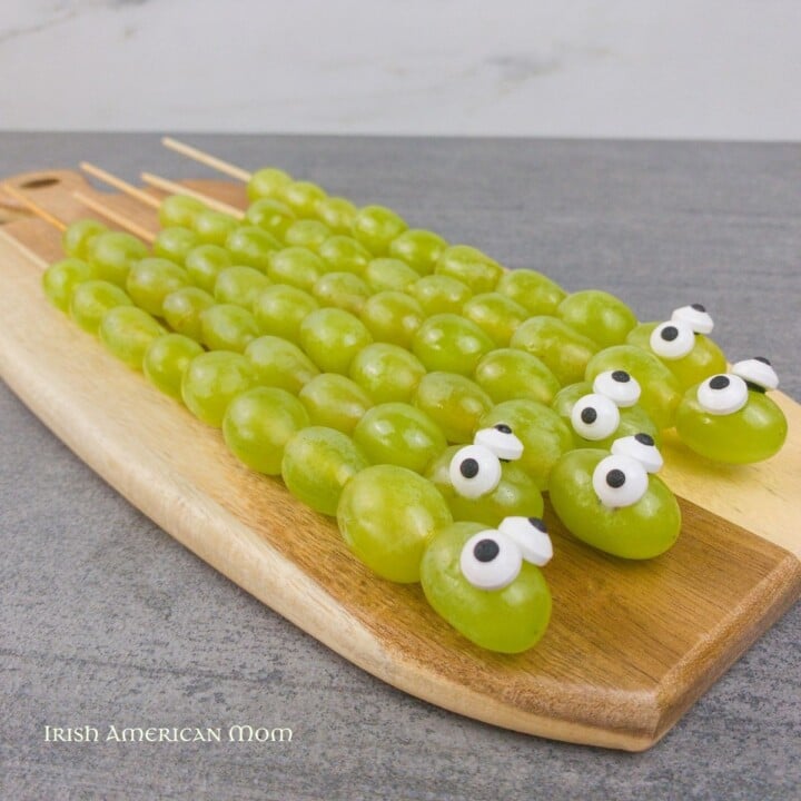 Grape snake snacks for Paddy's Day Featured Image | Irish American Mom Green grape snakes with candy eyes on a cutting board