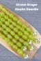 Green grapes threaded onto wooden skewers and decorated with candy eyes to resemble snakes, arranged on a wooden cutting board.