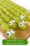 Close-up of green grape snakes with candy eyes lined up on a wooden board for a festive St. Patrickโs Day snack.