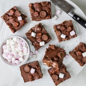 Slices of rocky road marshmallow chocolate cake on a plate with a knife and a bowl of mini marshmallows