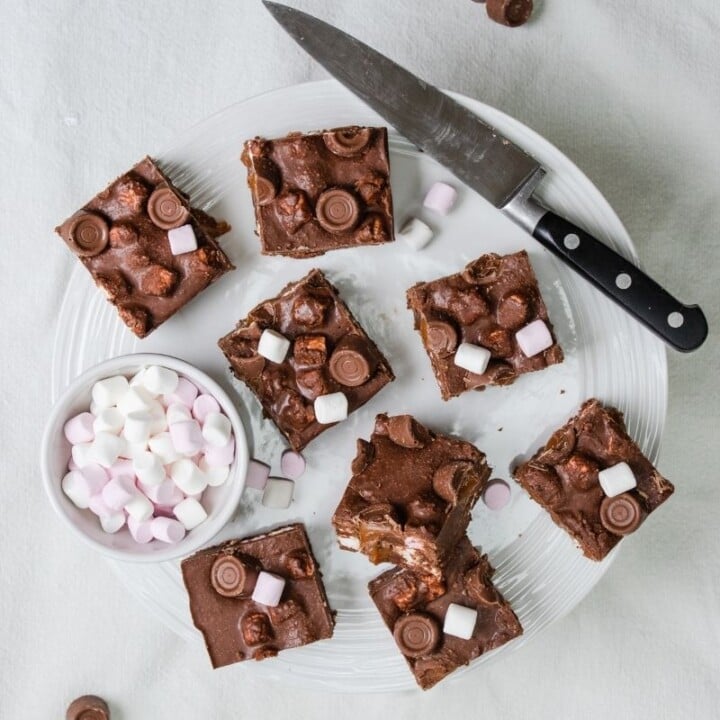 Rolo rocky roads cut into slices on a plate | Irish American Mom Square slices of chocolate and marshmallow cake on a plate with a knife and bowl of mini marshmallows