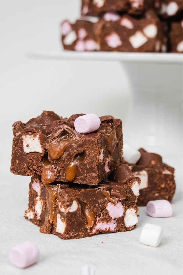 Rolo rocky roads with marshmallows and chocolate caramel candies | Irish American Mom Three pieces of chocolate, caramel and marshmallow cake beside slices of cake on a stand