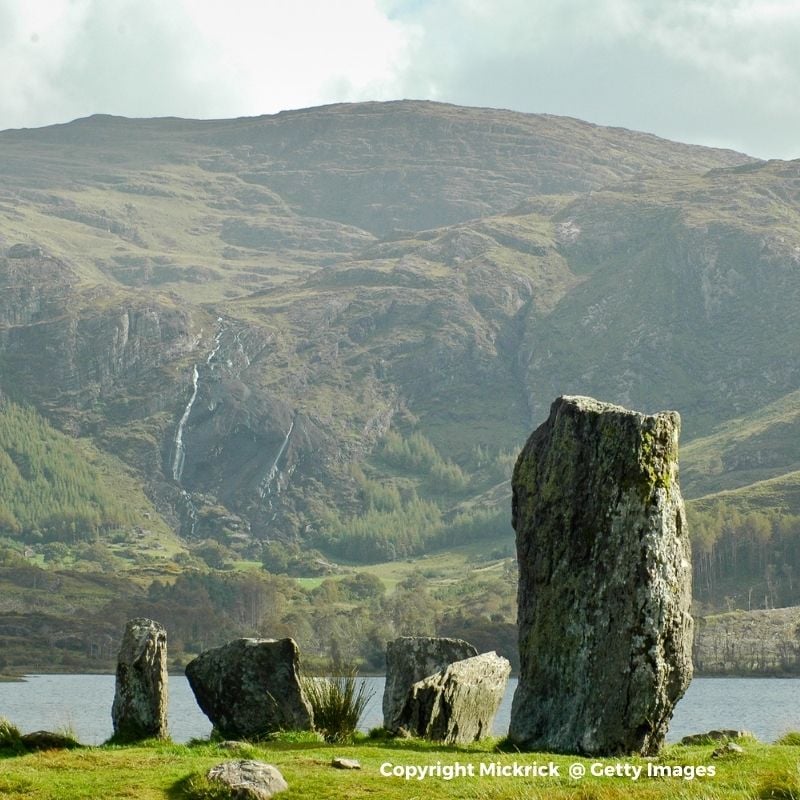 Standing stones at the water's edge with a mountain in the background