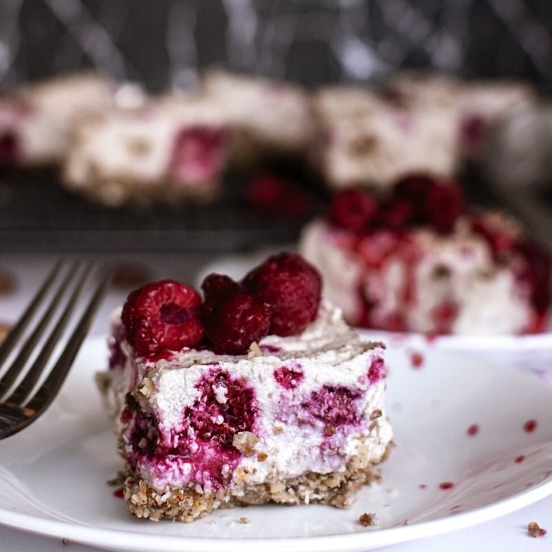 Vegan raspberry cheesecake slice on a plate | Irish American Mom Raspberry cheesecake on a white plate with a fork