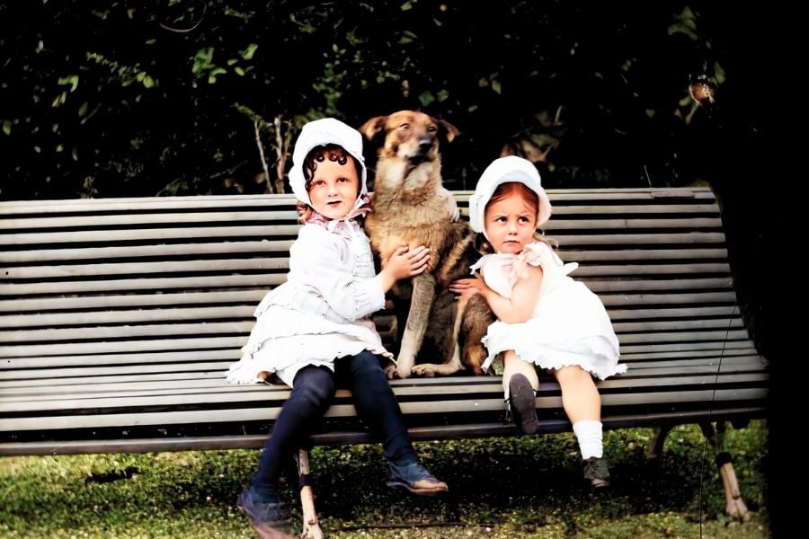 Two girls with a dog sitting on a bench
