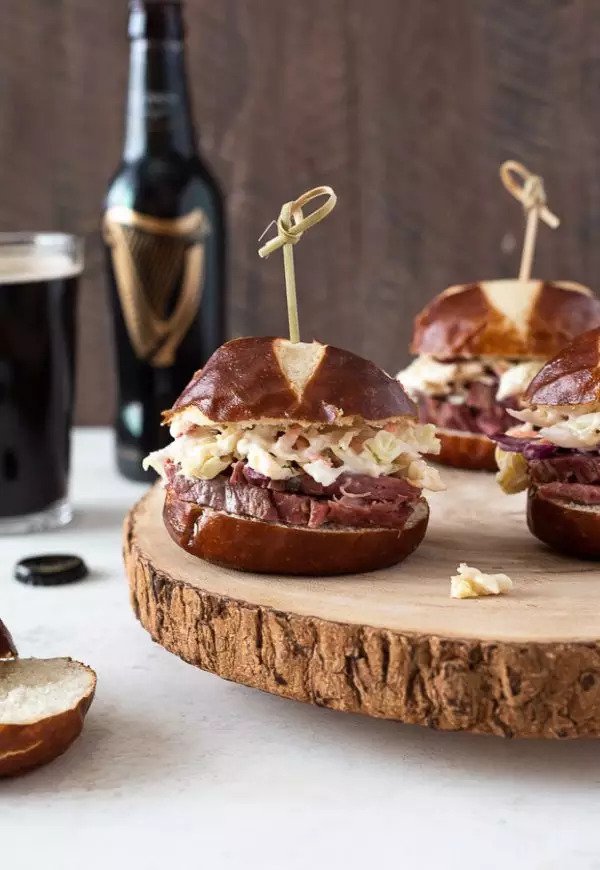 Corned beef slider sandwiches on a wooden round with a pint of Guinness and a bottle for Irish appetizers and party food