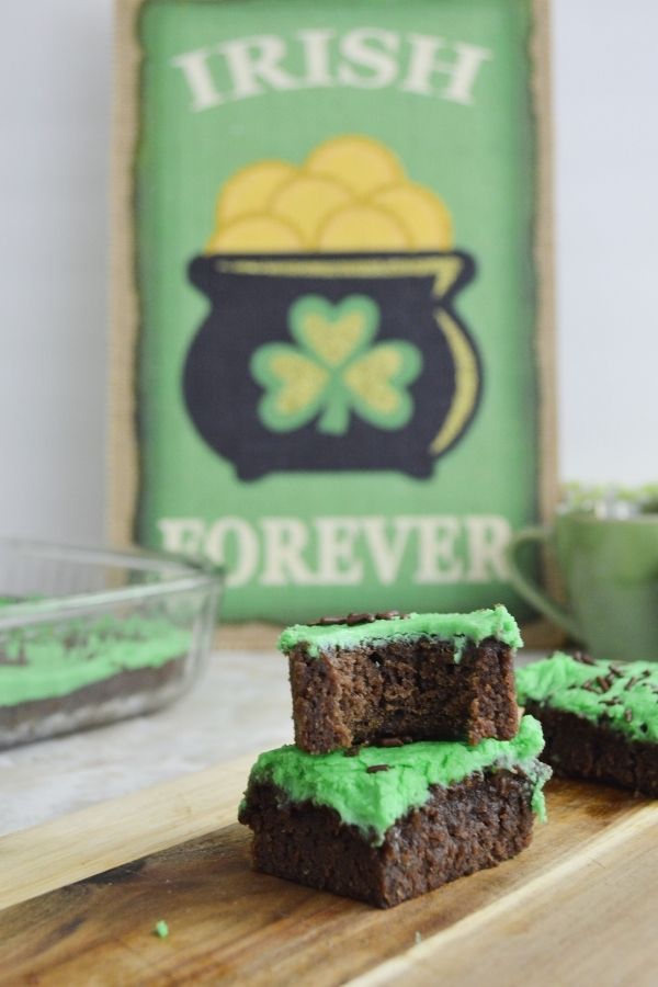 Green frosted Irish brownies | Irish American Mom A bit out of a brownie with green frosting in a stack beside a sign with a pot of gold
