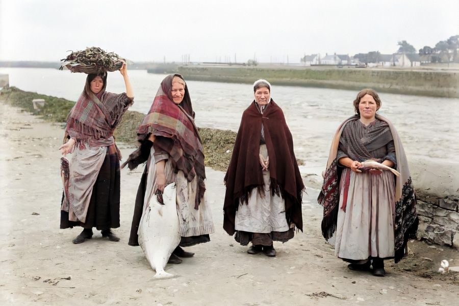 Women wearing shawls and holding fish beside a quay