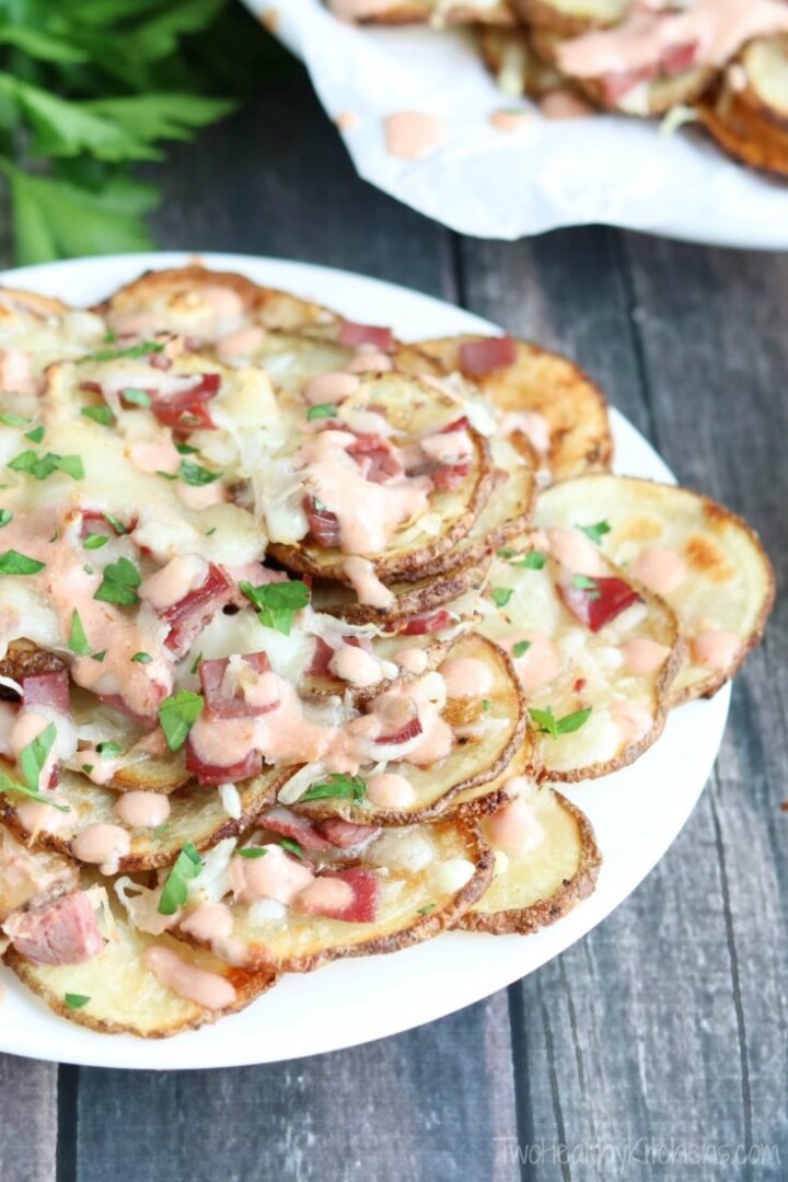 Sliced potatoes on a plate topped with dressings, melted cheese and corned beef pieces