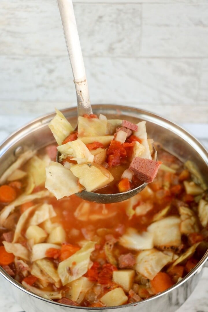 Left over corned beef and cabbage soup in a pot | Irish American Mom Serving a portion of hearty soup from a pot with a ladle
