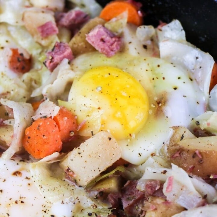 Left over corned beef hash being cooked in a skillet with egg | Irish American Mom Egg cooking in the middle of corned beef hash in a skillet