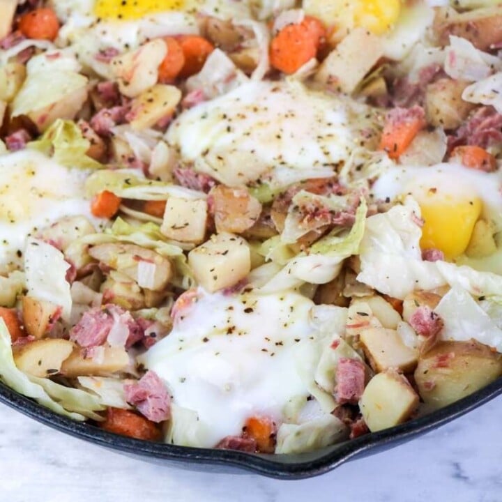 Left over corned beef hash being cooked in a skillet with eggs cooked on top | Irish American Mom Eggs on top of corned beef hash in a skillet