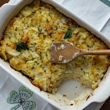 Looking down on a casserole dish of scalloped potatoes with a wooden spoon