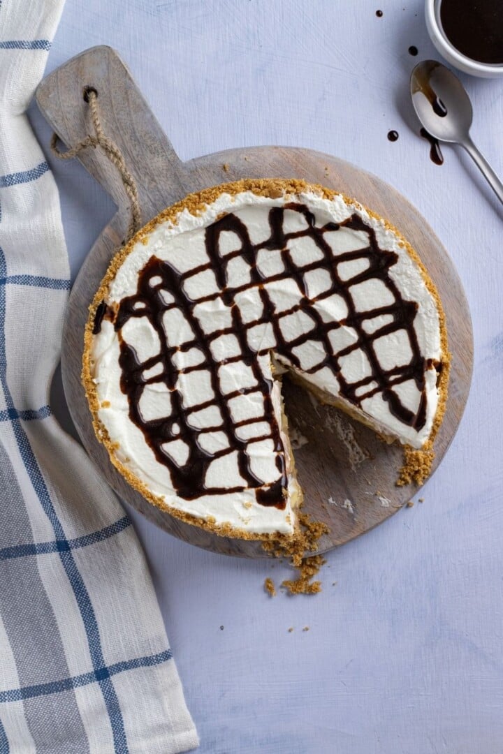 Chocolate drizzled on top of Banoffee Pie displayed on a cutting board | Irish American Mom Aerial shot of a cream cake with chocolate drizzle with a slice removed