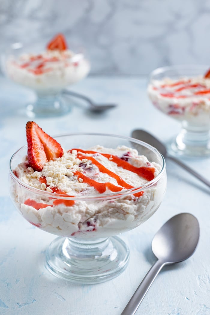 A bowl of Eton mess with strawberry sauce and a fresh strawberry | Irish American Mom Strawberry dessert in a glass bowl with a spoon