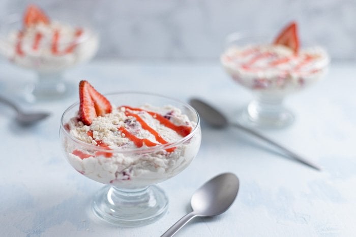 Three glass bowls with a strawberry cream dessert beside spoons