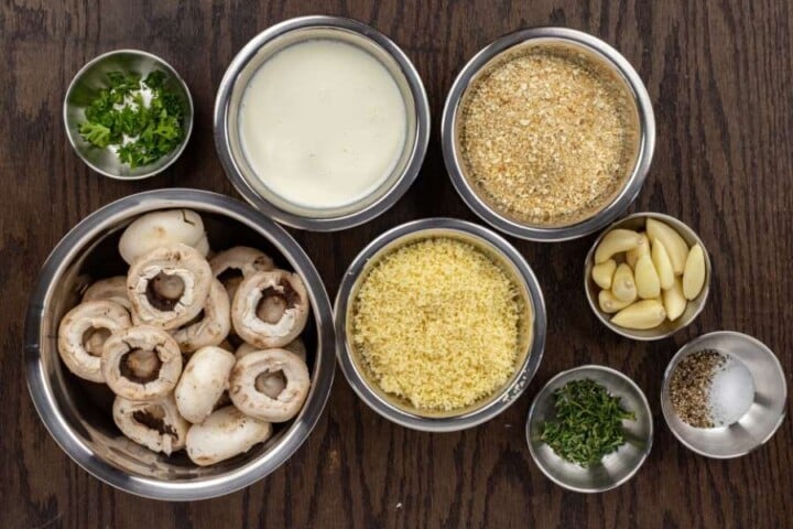 Ingredients for cheese stuffed mushrooms | Irish American Mom Mushrooms, cream, garlic cloves, grated cheese, breadcrumbs and herbs in bowls